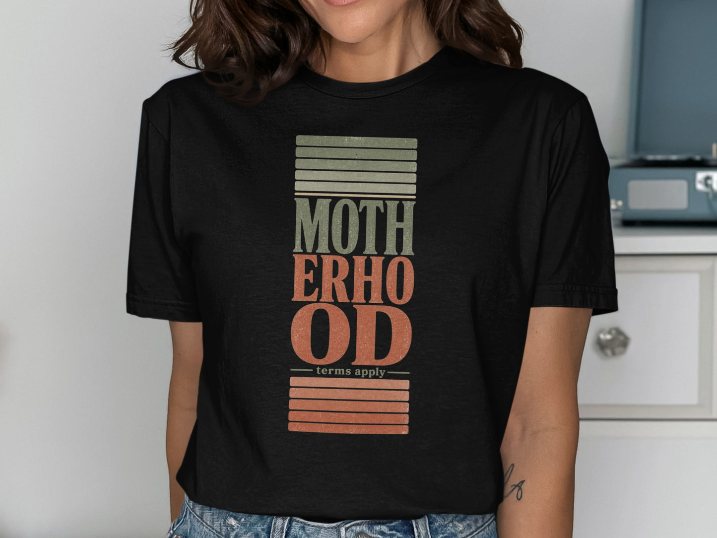 Black t-shirt with "MOTHERHOOD" text and "terms apply" with textured stripes.