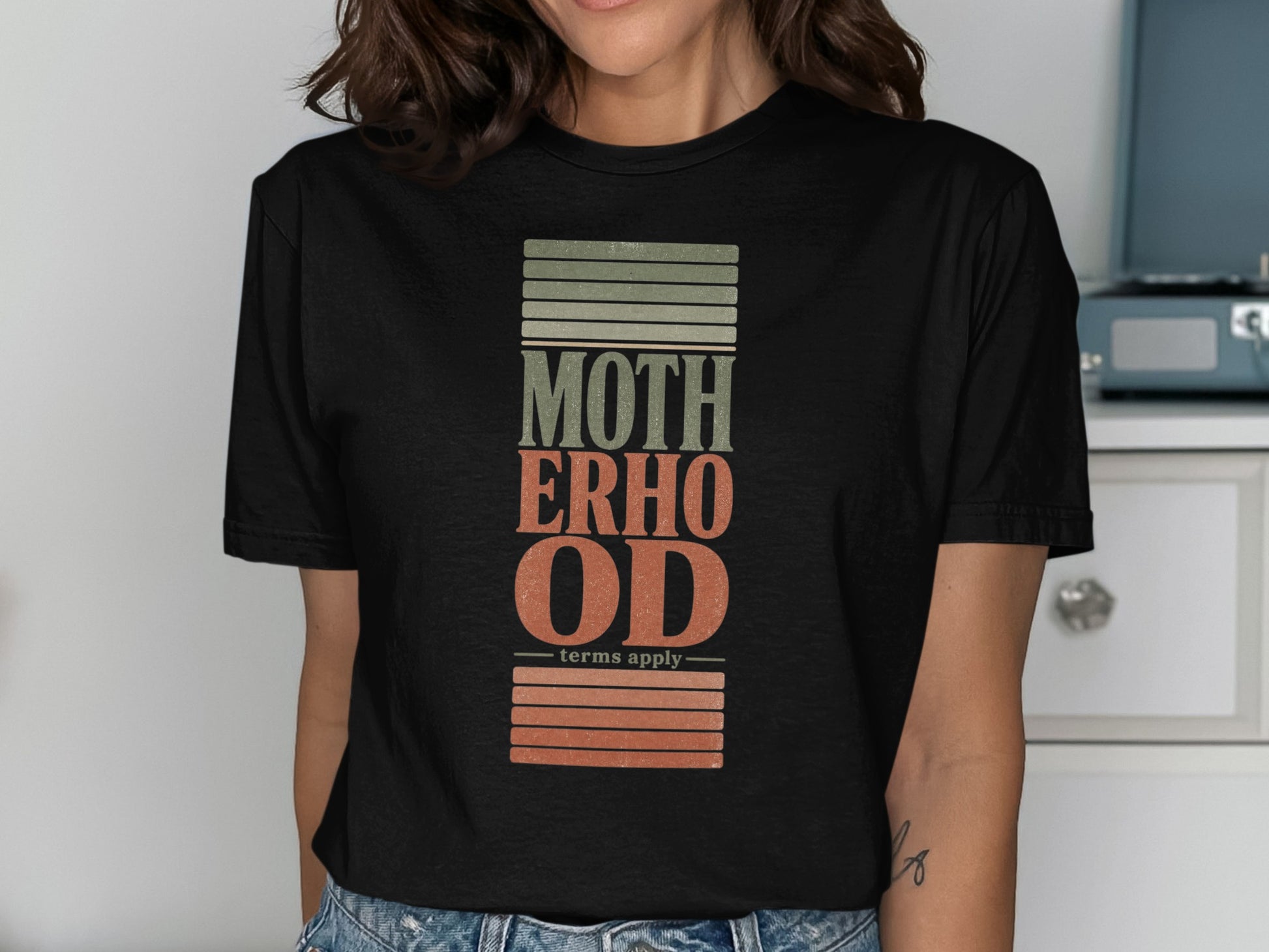 Black t-shirt with "MOTHERHOOD" text and "terms apply" with textured stripes.