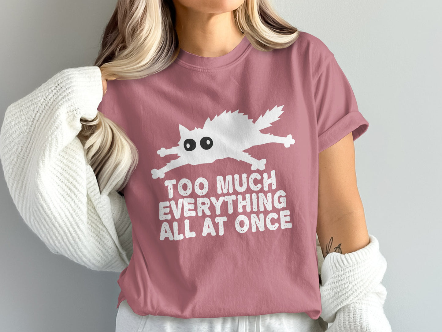 Pink t-shirt with white cartoon cat and text "TOO MUCH EVERYTHING ALL AT ONCE".