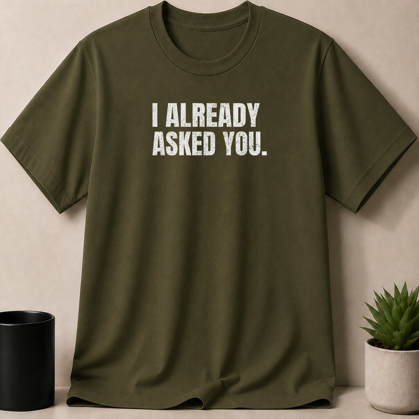 Olive green t-shirt with white distressed text reading "I ALREADY ASKED YOU."