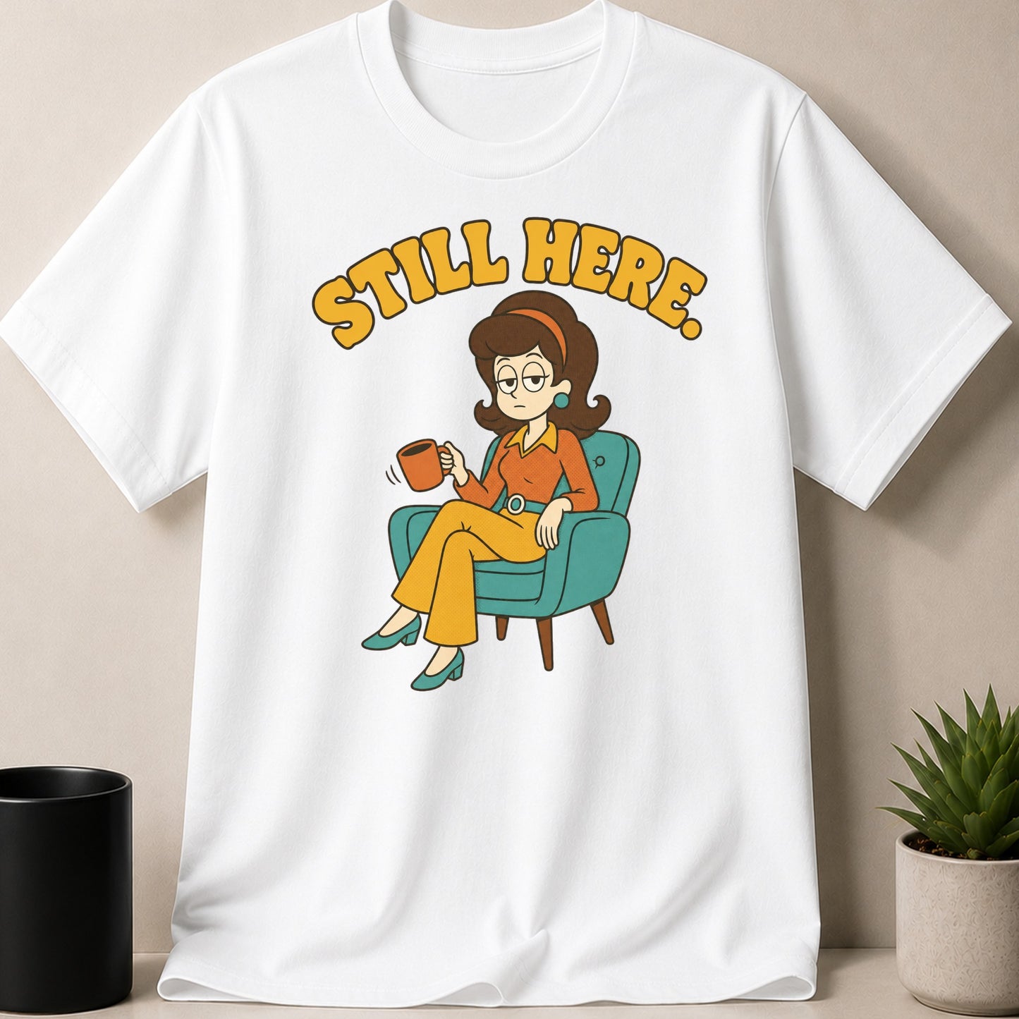 White t-shirt with cartoon of woman in chair holding mug, text "STILL HERE."