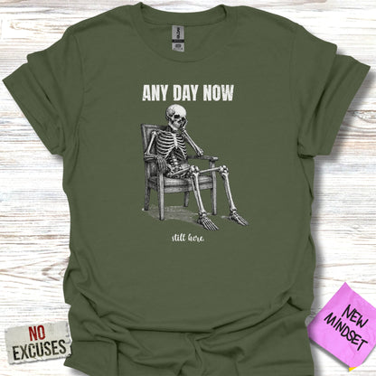 Olive green t-shirt with a skeleton sitting in a chair and text "ANY DAY NOW still here".