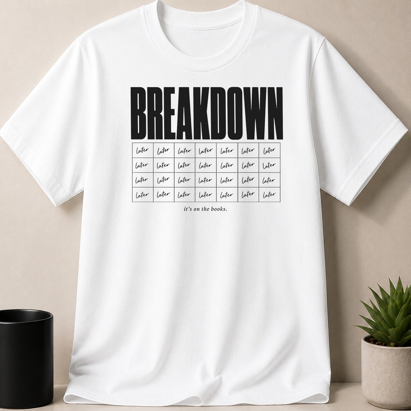 White t-shirt with black text "BREAKDOWN" and rows of "later" in boxes.