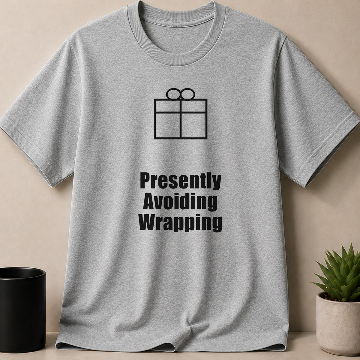 Gray short-sleeved t-shirt featuring a black gift box graphic and the text "Presently Avoiding Wrapping".