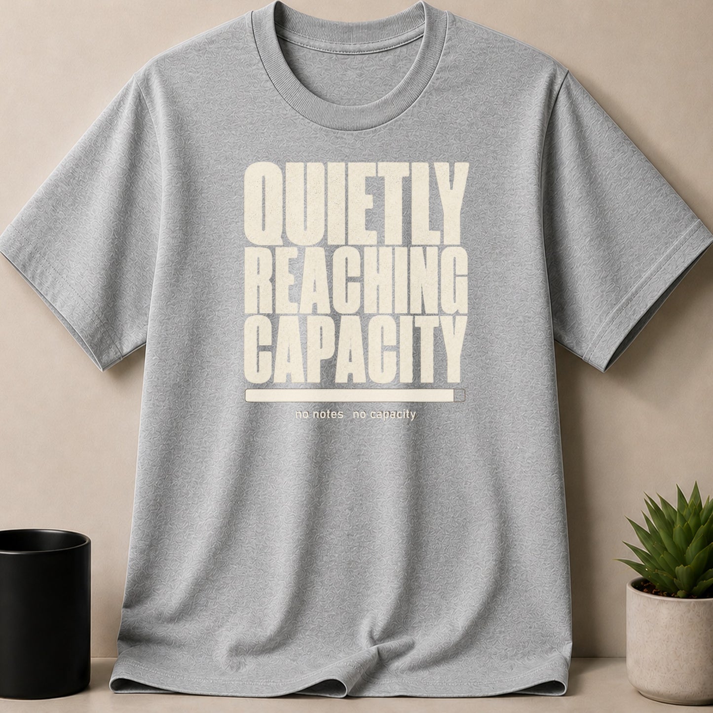 Grey t-shirt with text "QUIETLY REACHING CAPACITY" and a loading bar.