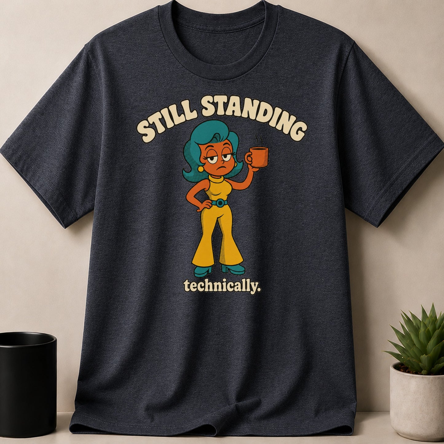 Dark grey t-shirt with cartoon woman, coffee cup, and text "Still Standing Technically."