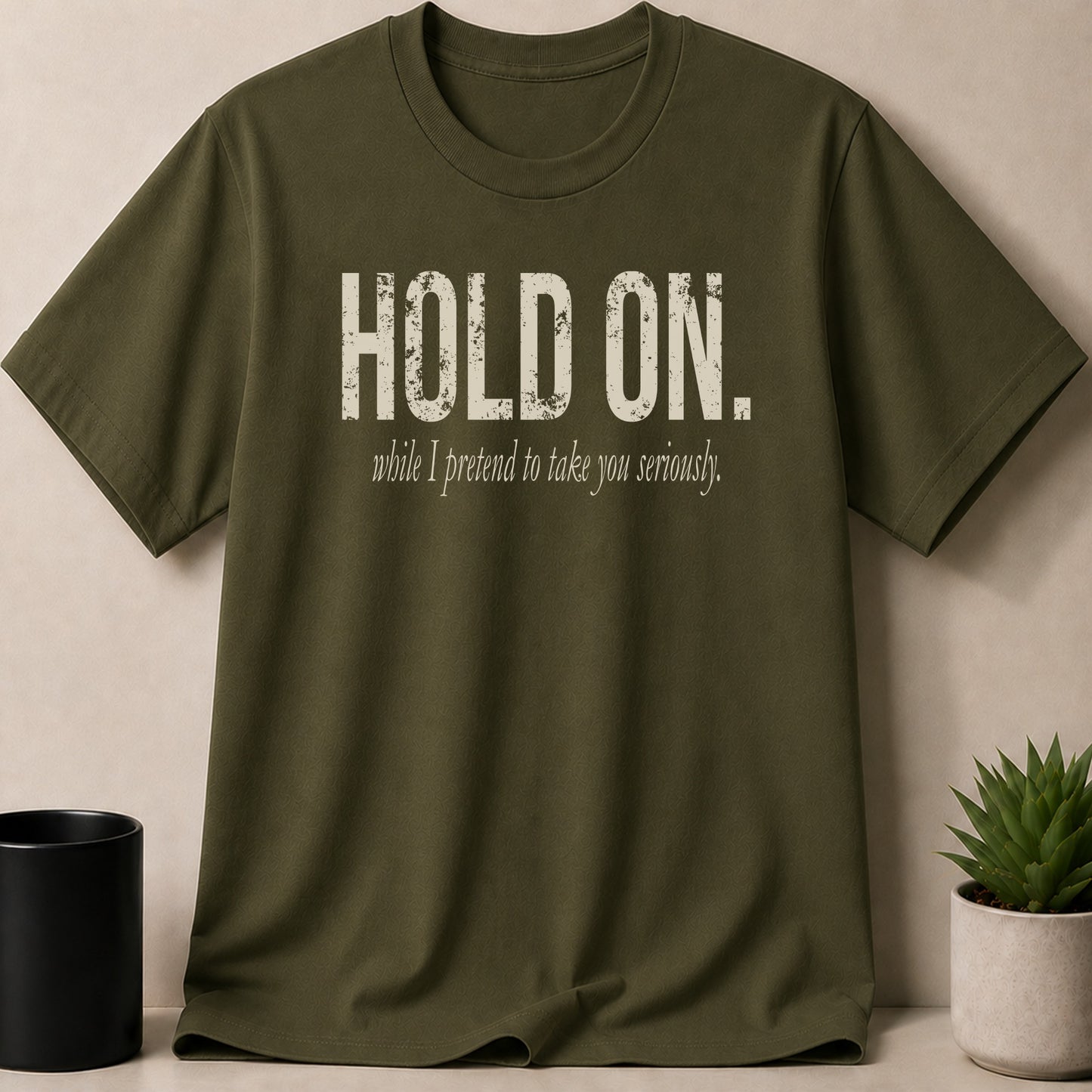 Olive green t-shirt with distressed white text that reads "HOLD ON. while I pretend to take you seriously."