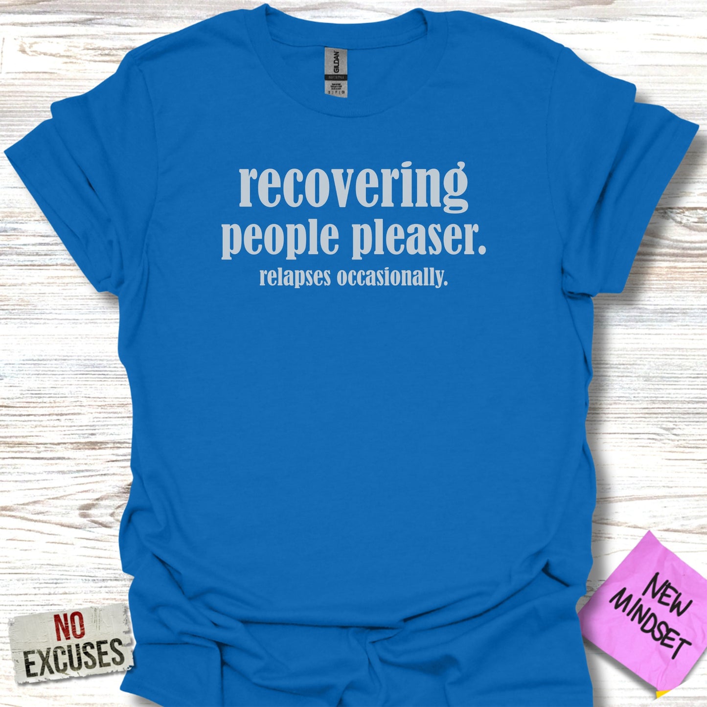 Blue t-shirt with white text "Recovering people pleaser. relapses occasionally." and "NEW MINDSET" label.