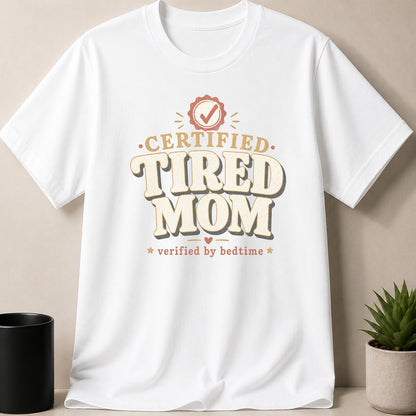 White t-shirt with "Certified Tired Mom Verified by Bedtime" text and graphic.