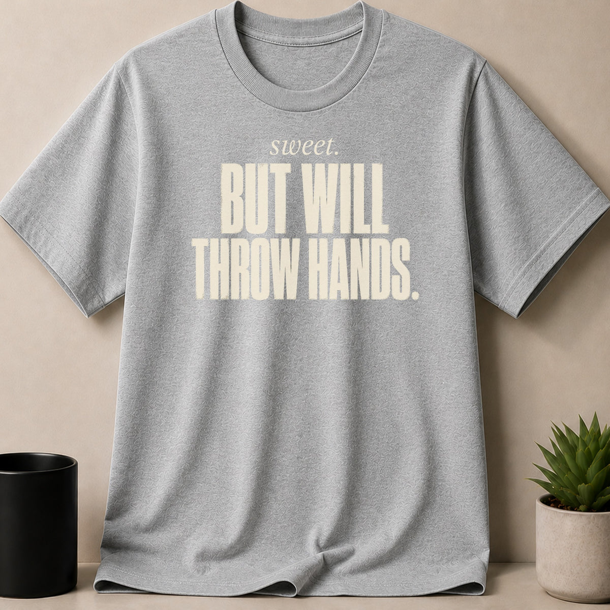 Grey t-shirt with beige text "sweet. BUT WILL THROW HANDS."