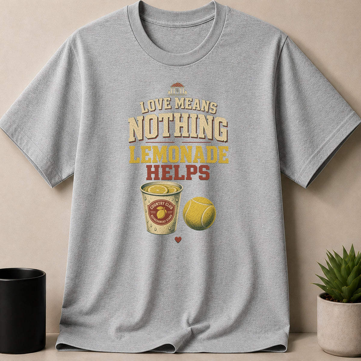 Grey t-shirt with "Love Means Nothing Lemonade Helps" text, cup of lemonade, and tennis ball.