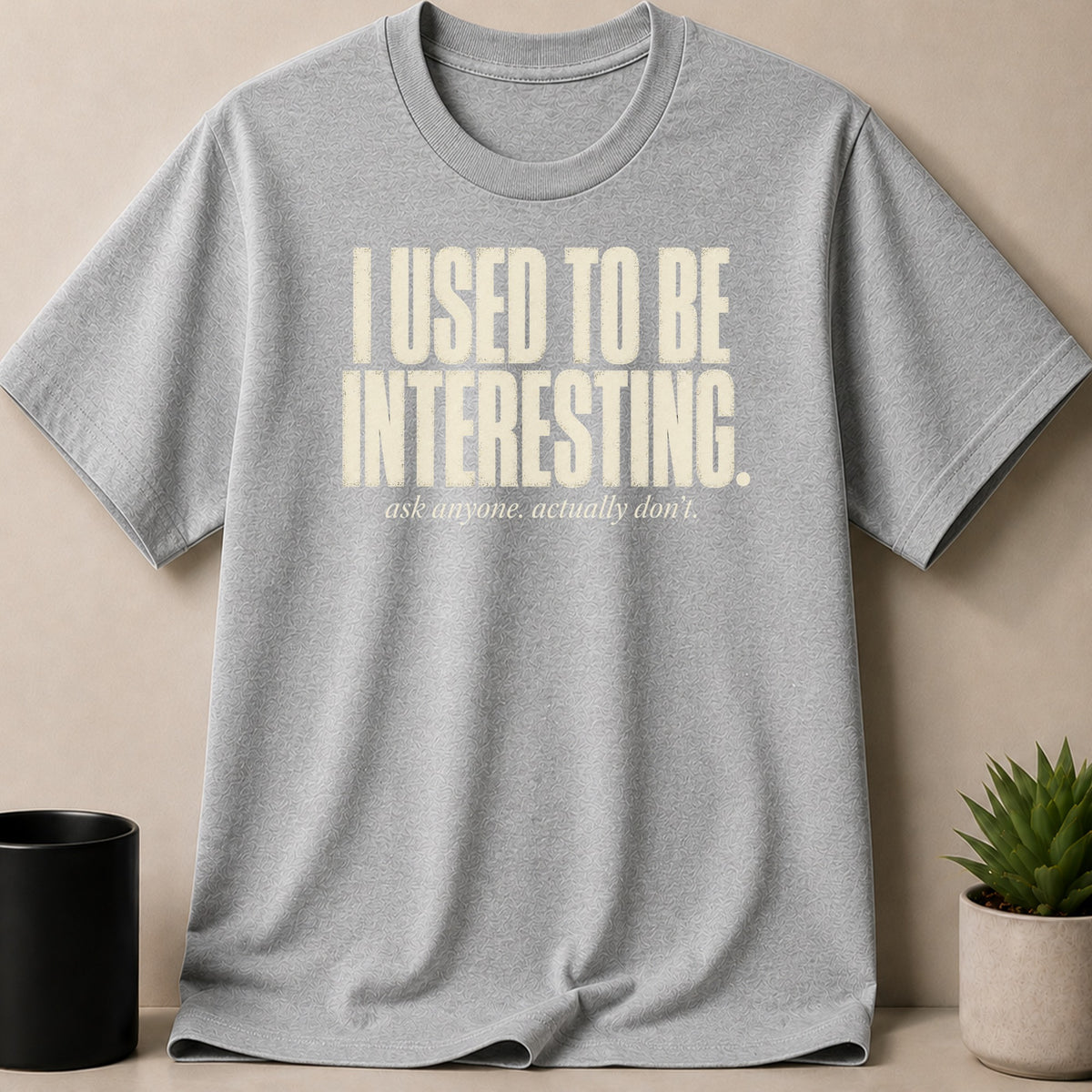 Grey t-shirt with text "I USED TO BE INTERESTING. ask anyone. actually don't." in cream.