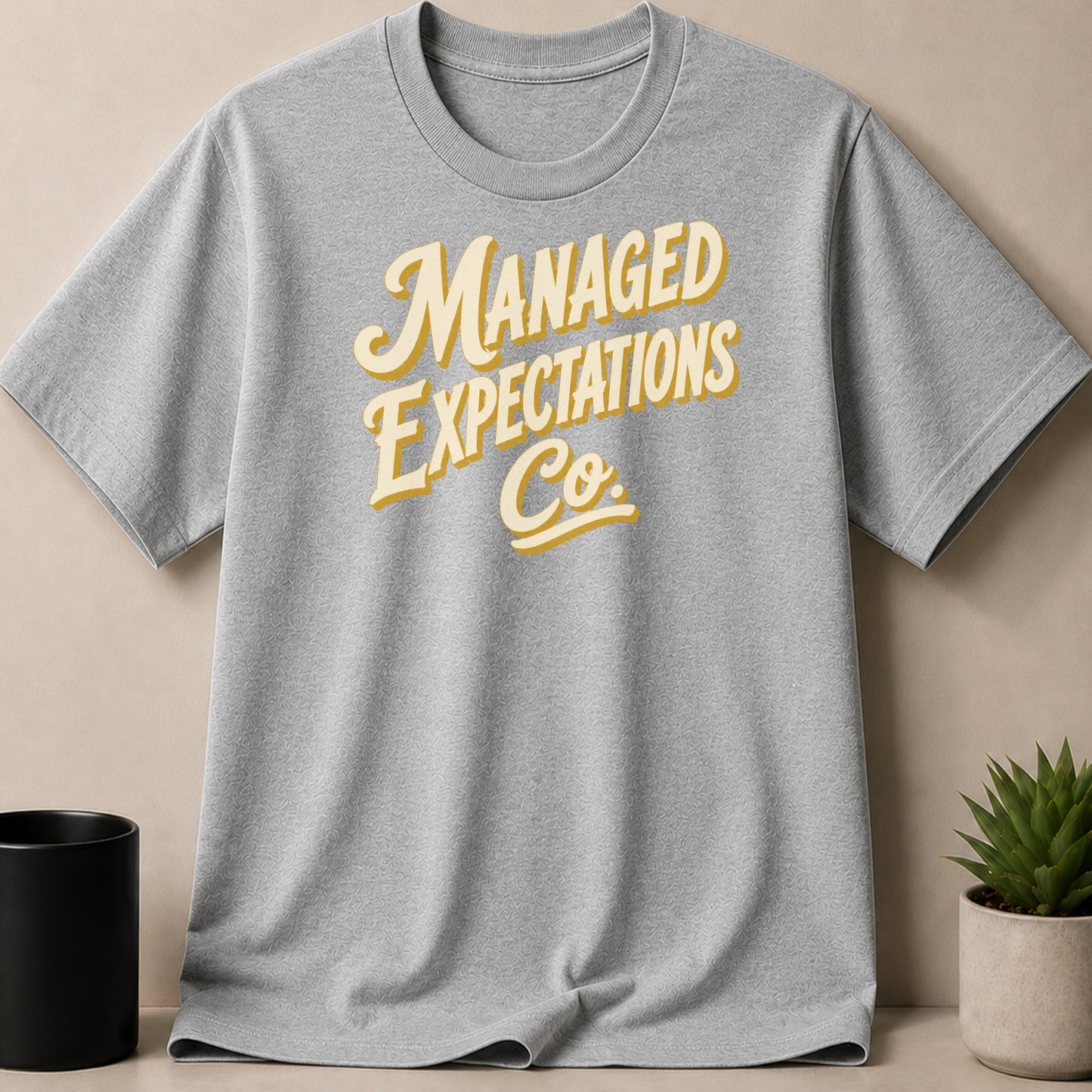 Grey t-shirt with yellow and cream text "MANAGED EXPECTATIONS Co."