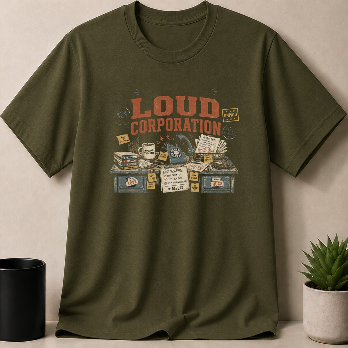 Olive green t-shirt with "LOUD CORPORATION" print, featuring a desk with office supplies.