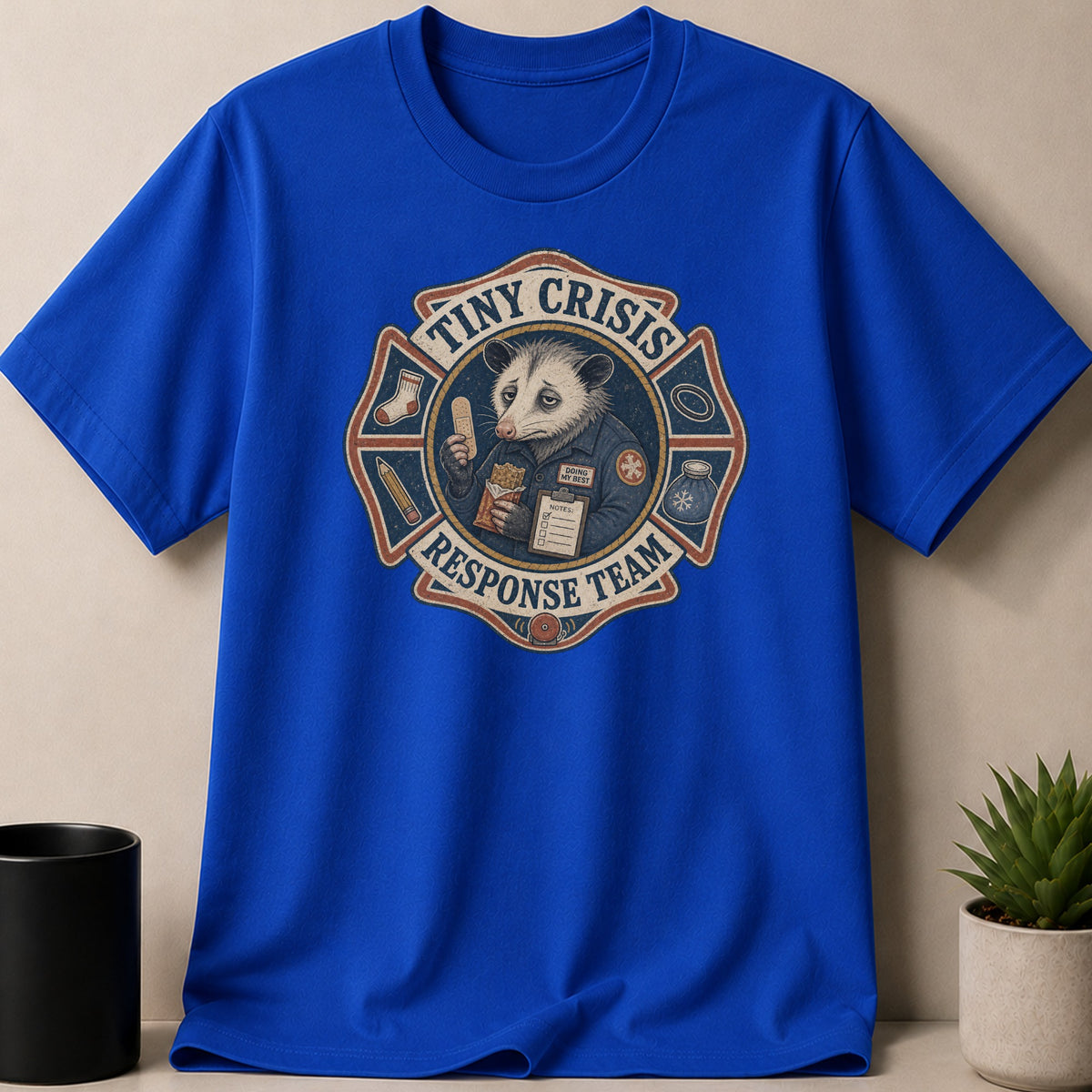 Blue t-shirt with opossum in fire badge graphic reading "Tiny Crisis Response Team".
