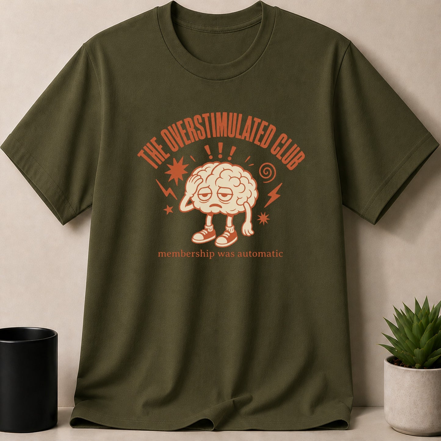 Green t-shirt with "The Overstimulated Club" text and a cartoon brain graphic.