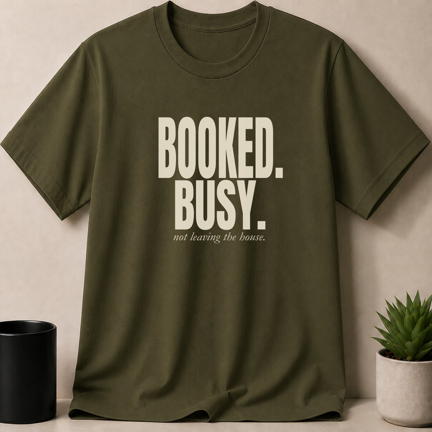 Olive green t-shirt with "BOOKED. BUSY. not leaving the house." text.