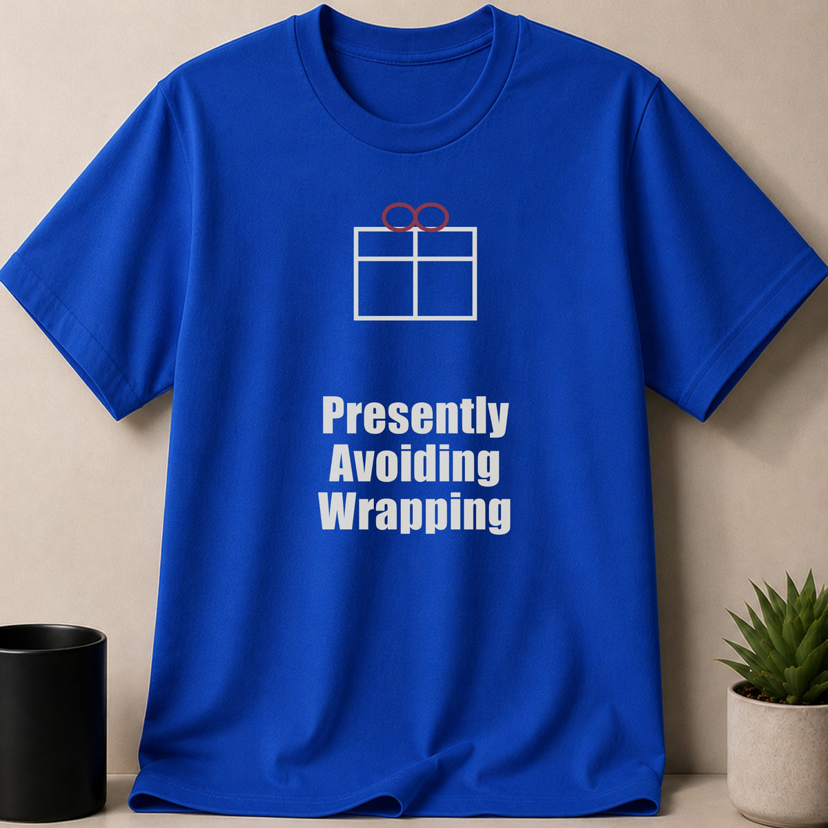A blue short-sleeve t-shirt with a white graphic of a wrapped gift and the white text Presently Avoiding Wrapping.