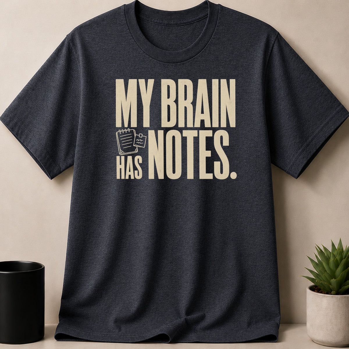 Dark t-shirt with cream text "MY BRAIN HAS NOTES." and small notepad graphic.