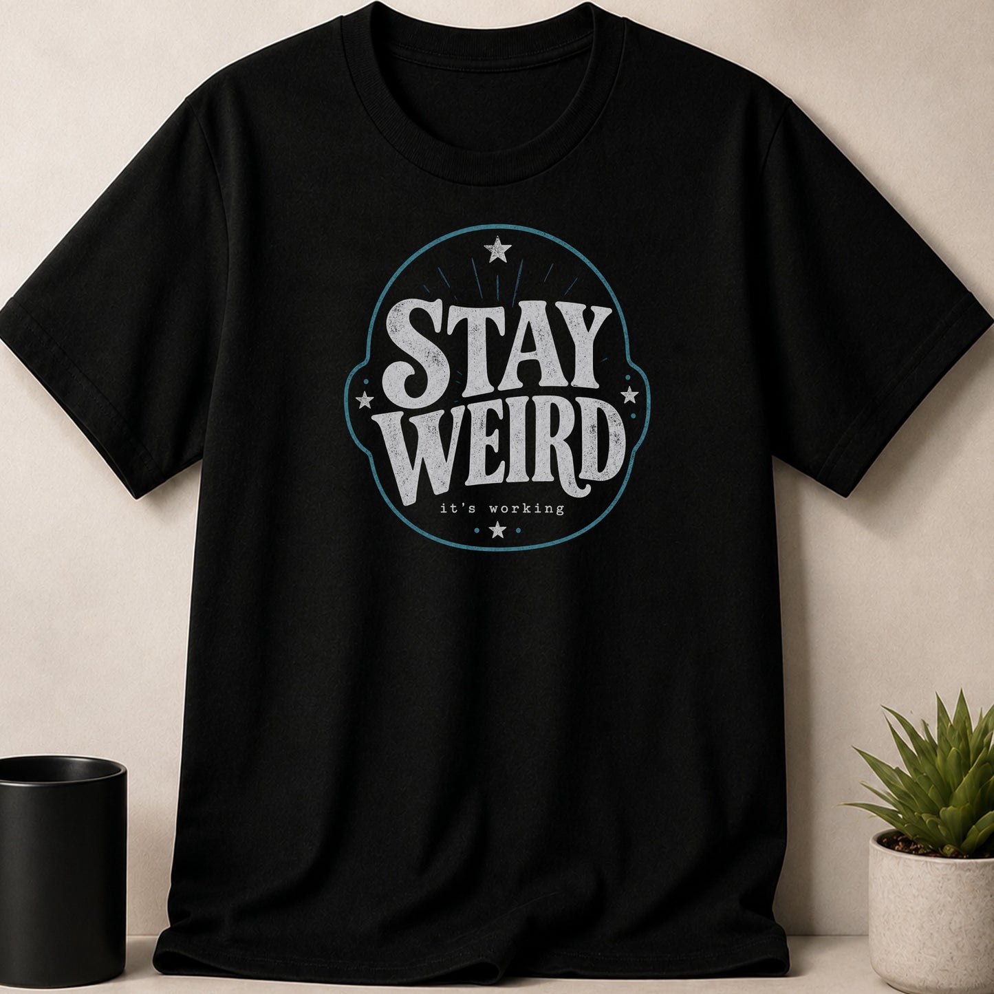Black t-shirt with distressed "STAY WEIRD it's working" text and star design.