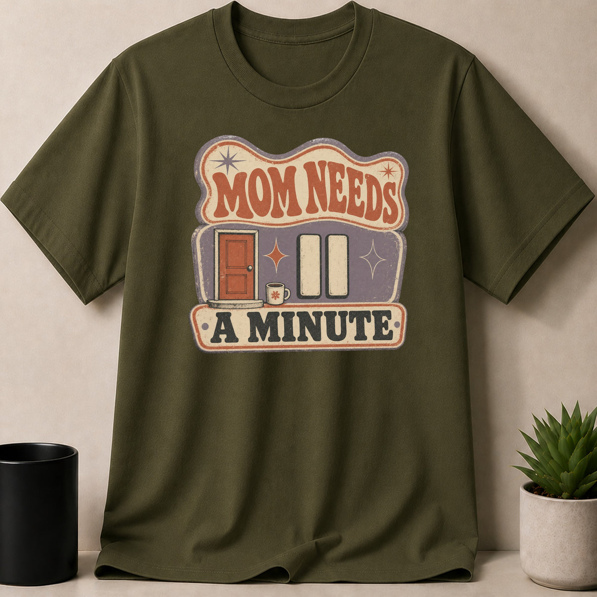 Olive green t-shirt with "Mom Needs A Minute" graphic including a door and coffee mug.
