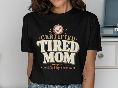 Black t-shirt with "Certified Tired Mom verified by bedtime" text and graphics.