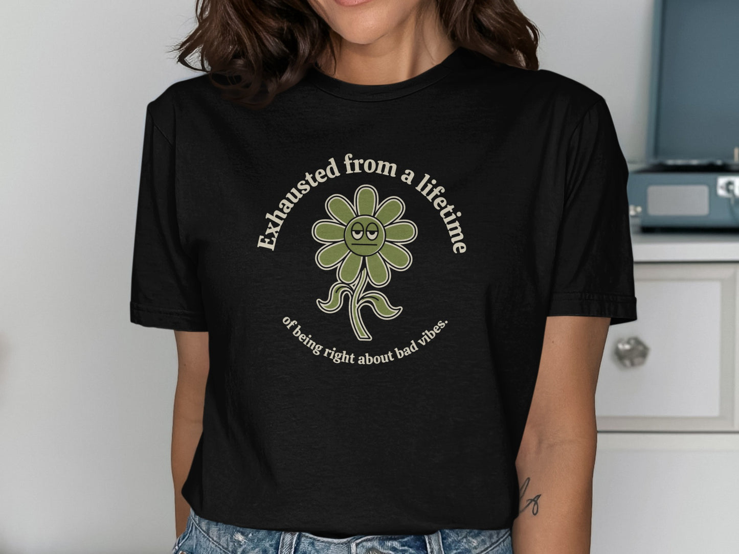 Black t-shirt with a green flower graphic and text reading "Exhausted from a lifetime of being right about bad vibes."