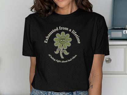 Black t-shirt with a green flower graphic and text reading "Exhausted from a lifetime of being right about bad vibes."