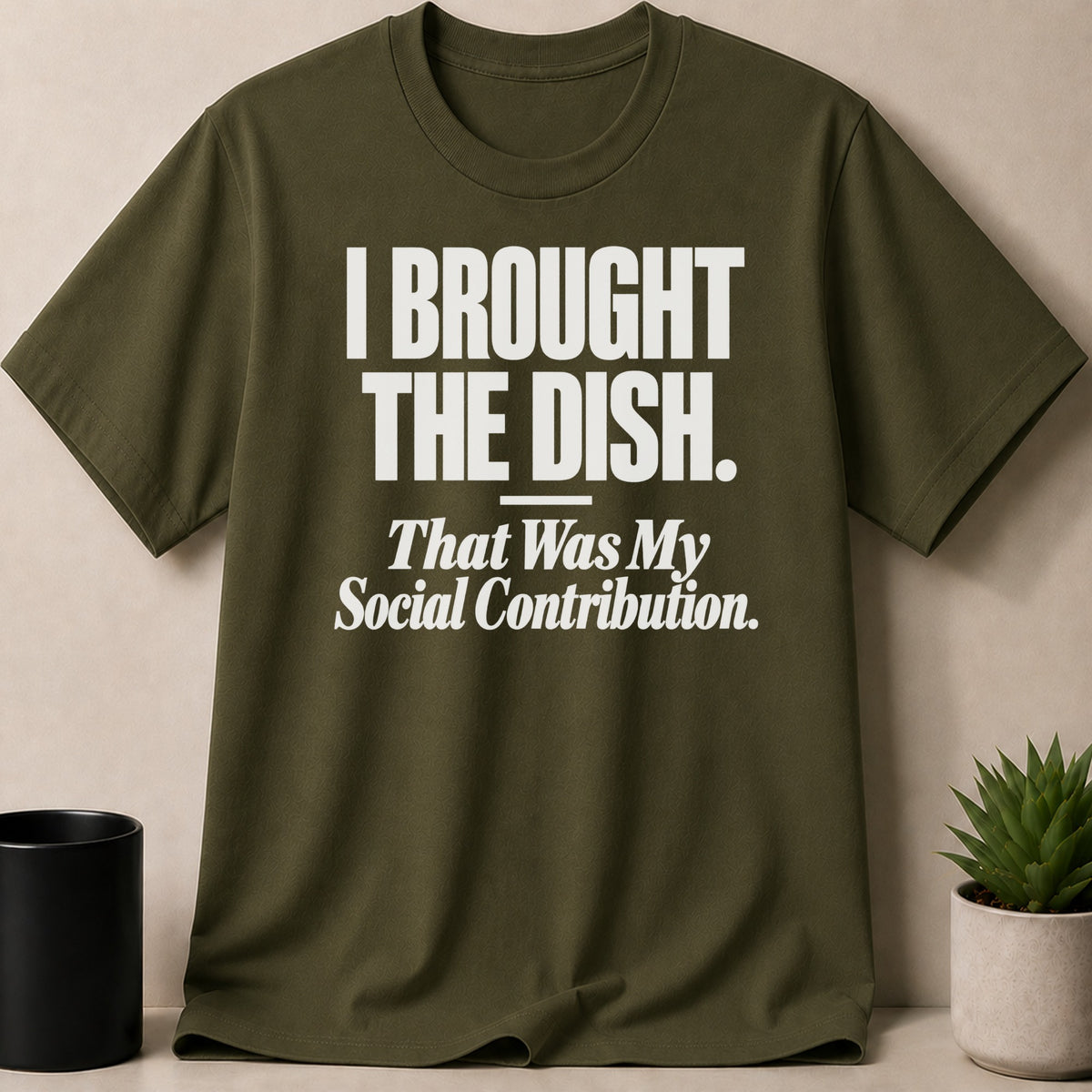 An olive green crewneck t-shirt with white text reading I BROUGHT THE DISH. That Was My Social Contribution.