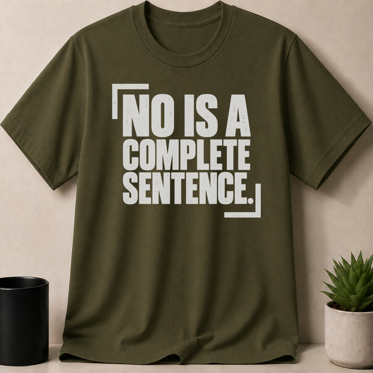 An olive green t-shirt with white text that reads NO IS A COMPLETE SENTENCE.