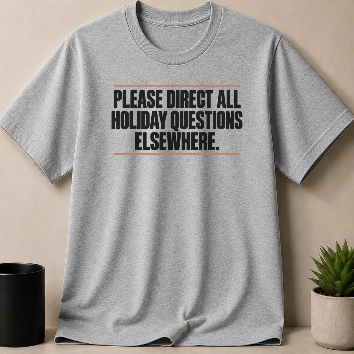 A grey short-sleeved t-shirt with the black text PLEASE DIRECT ALL HOLIDAY QUESTIONS ELSEWHERE centered on the chest.