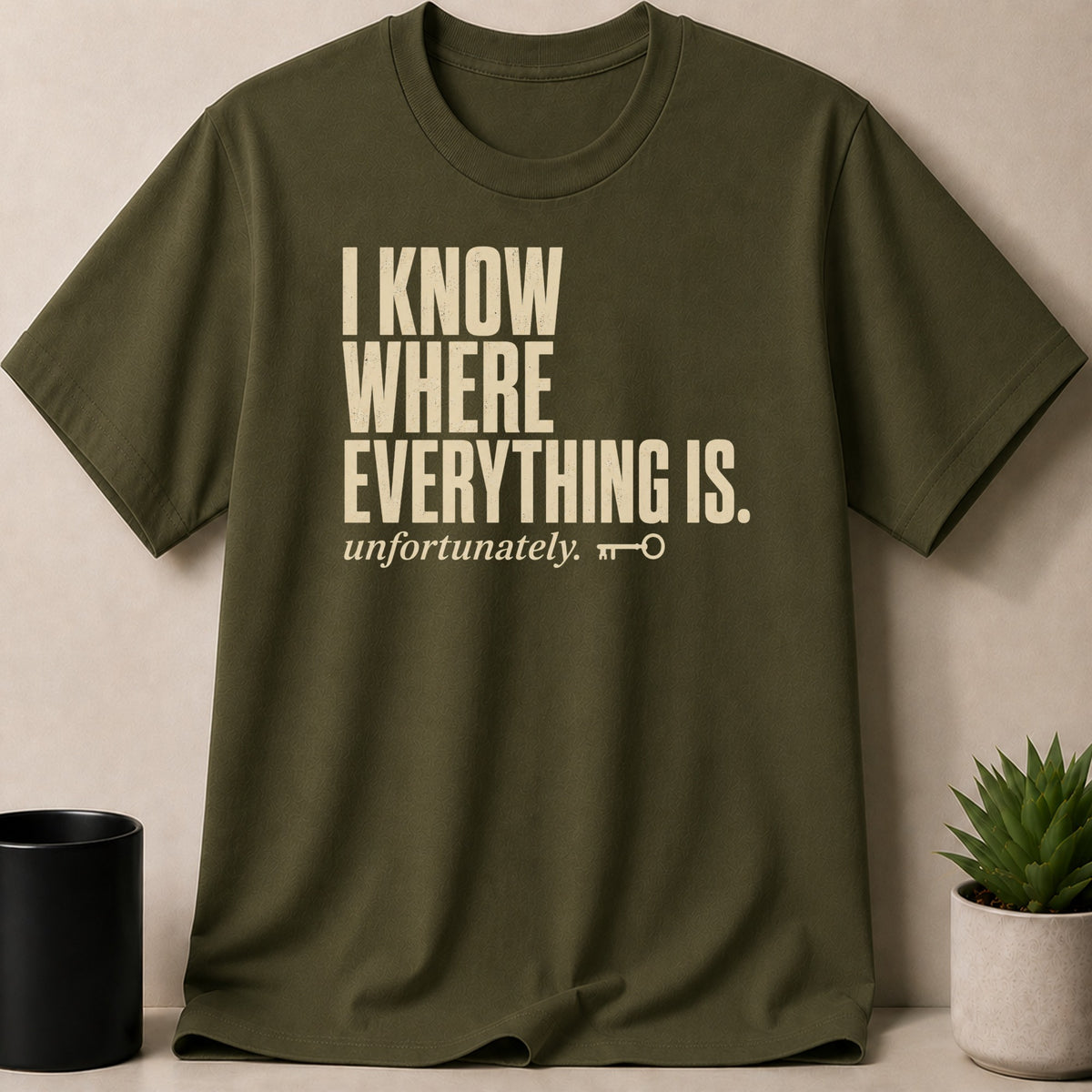 Olive green t-shirt with cream text "I KNOW WHERE EVERYTHING IS. unfortunately." and a key icon.