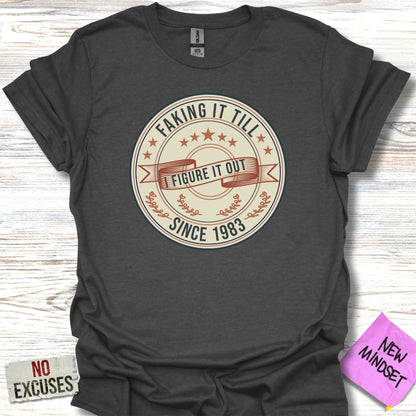 Dark grey t-shirt with "Faking it till I figure it out since 1983" graphic.