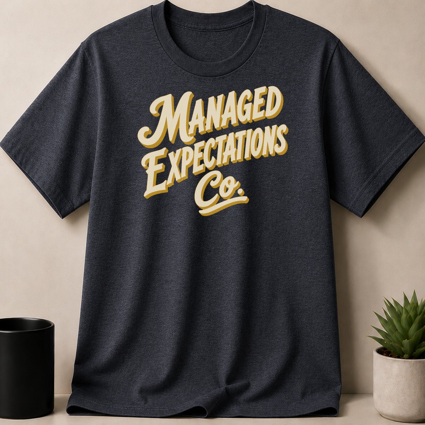 Dark grey t-shirt with "Managed Expectations Co." text in yellow and white.