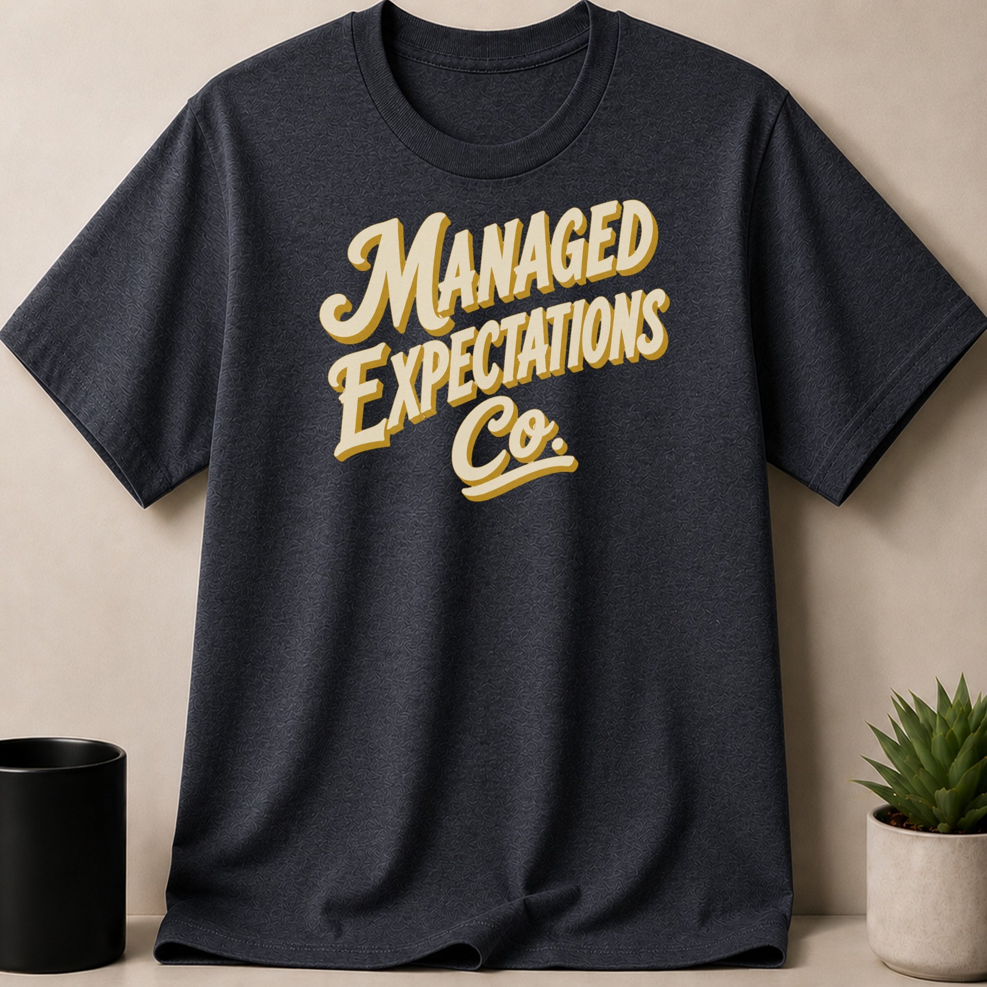 Dark grey t-shirt with "Managed Expectations Co." text in yellow and white.