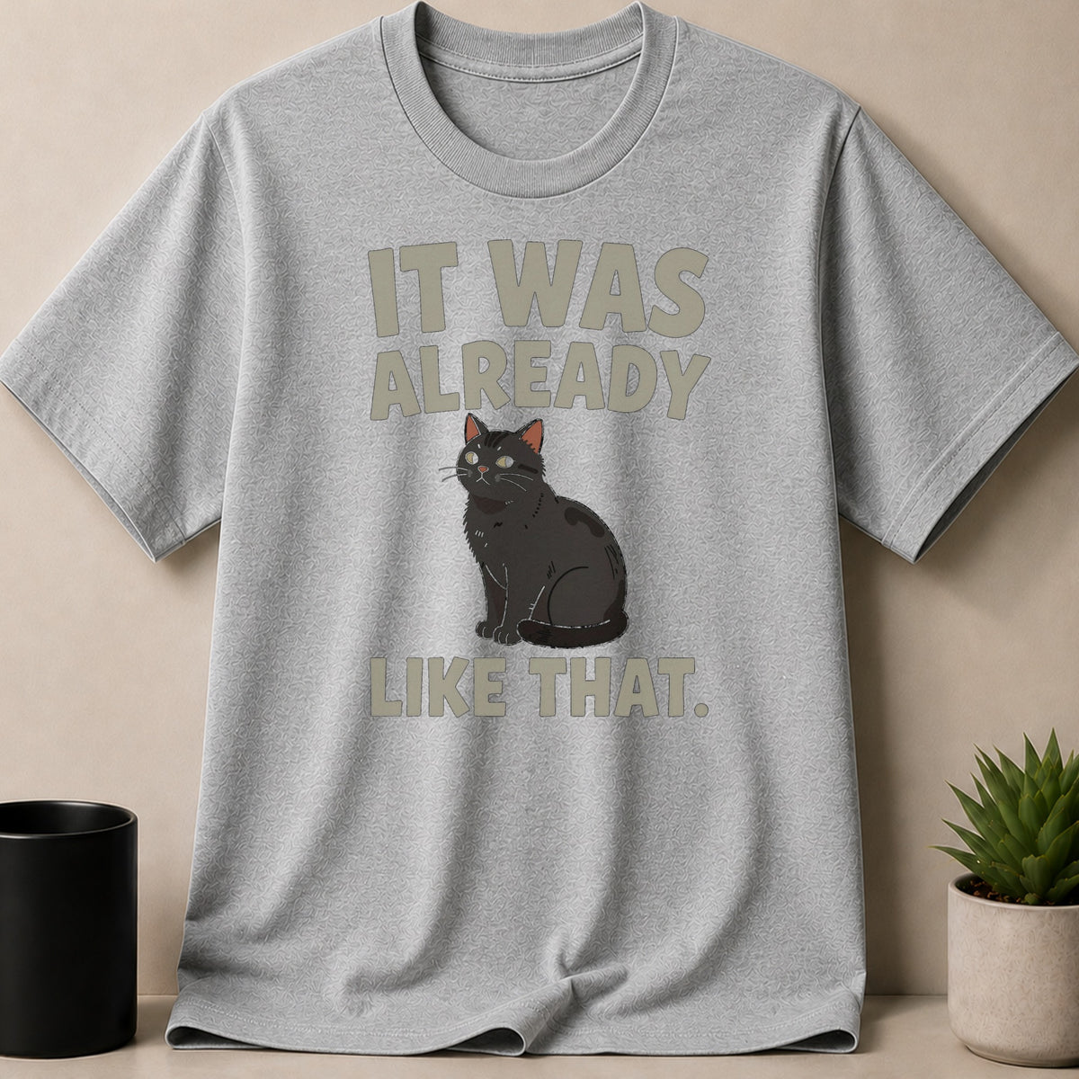 A grey crew-neck t-shirt displays an illustration of a black cat and the text IT WAS ALREADY LIKE THAT.