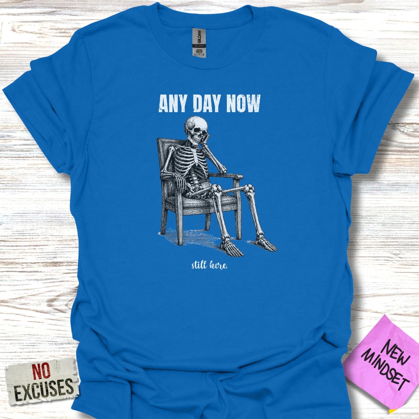 Blue t-shirt with skeleton sitting in chair, text "ANY DAY NOW still here".