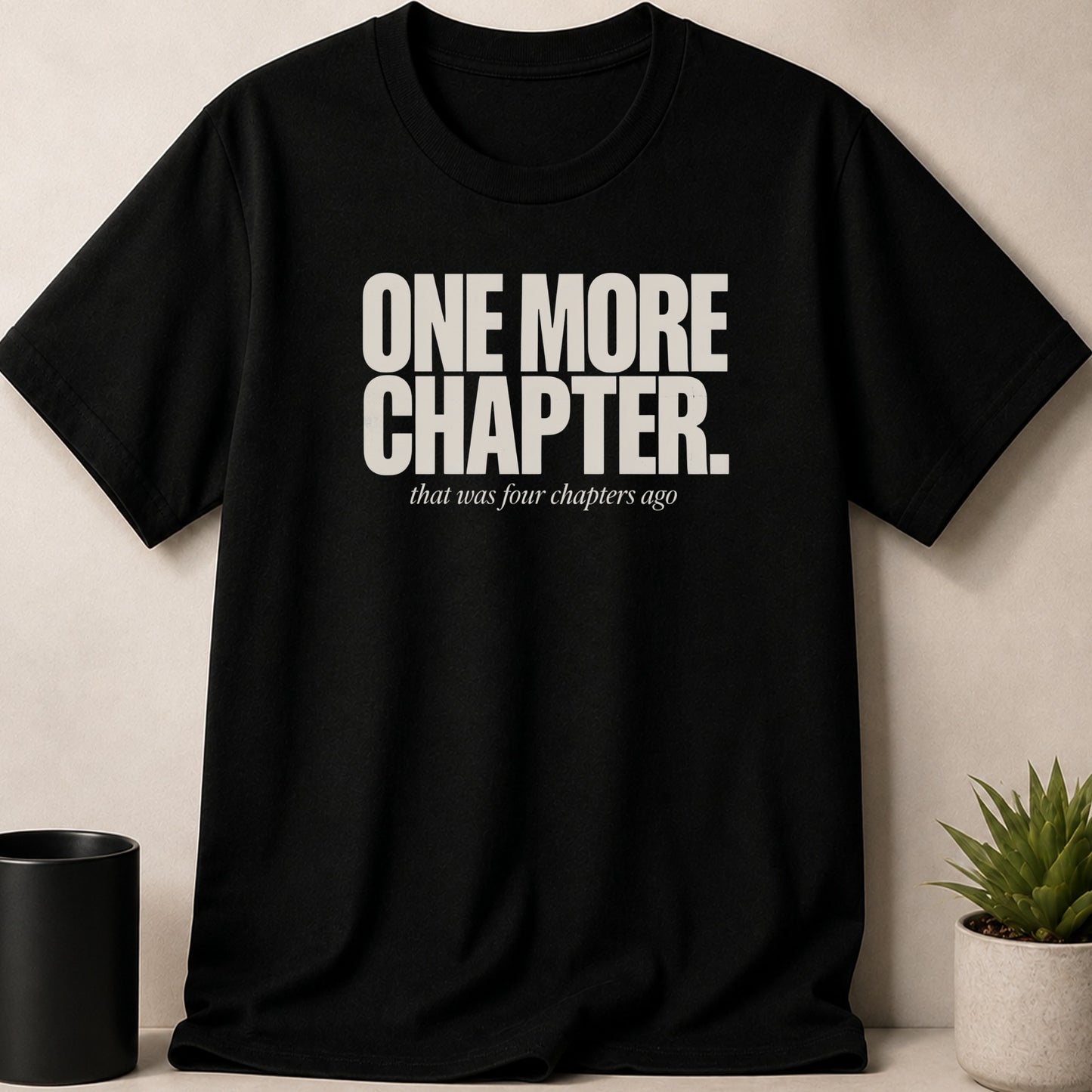 Black t-shirt with white text "ONE MORE CHAPTER that was four chapters ago".